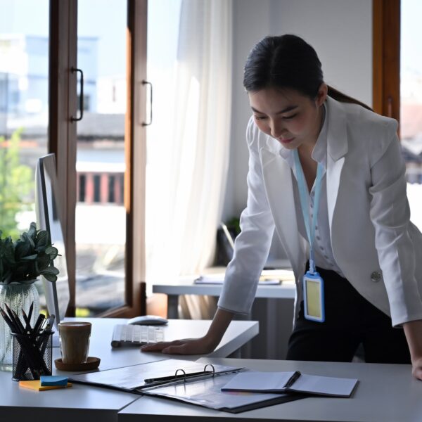 Attractive businesswoman standing at her office desk and reading information on notebook.