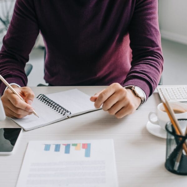cropped image of designer in burgundy sweater writing something to notebook in office